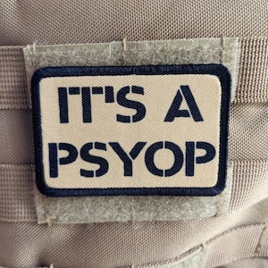 May include: A tan tactical vest with a black patch that reads "IT'S A PSYOP".