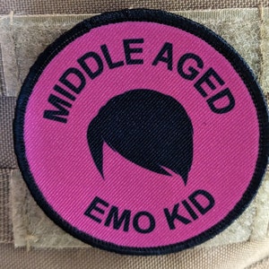 Può includere: Un cerotto rotondo rosa e nero con il testo "Middle Aged Emo Kid" e una silhouette nera di una persona con la frangia laterale.