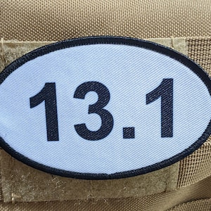 Puede incluir: Parche ovalado blanco con borde negro y el número "13.1" impreso en negro.