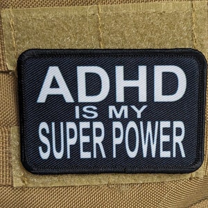 以下が含まれることがあります： 茶色の背景に「ADHD is my super power」という文字が書かれた白黒のパッチ