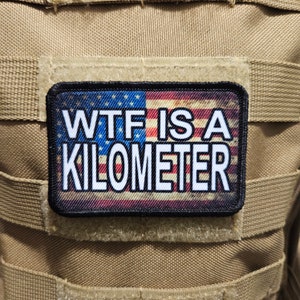 May include: A black and white patch with an American flag background. The text "WTF IS A KILOMETER" is printed in white on the patch.