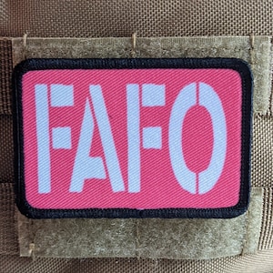 Könnte beinhalten: Ein rosa Patch mit schwarzen Nähten und einem weißen Umriss. Der Patch sagt "FAFO" in weißen Buchstaben.
