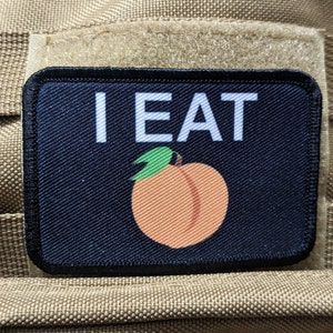 Puede incluir: Un parche negro con texto blanco que dice "I EAT" y un melocotón con una hoja verde sobre un fondo negro.