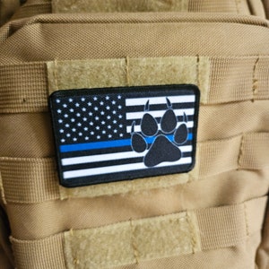 May include: A black and white American flag patch with a blue stripe and a black paw print. The patch is sewn onto a tan tactical bag.