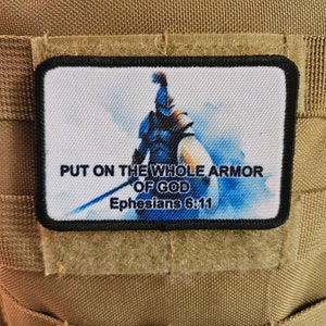May include: A white patch with a blue and white image of a warrior with a sword. The text "PUT ON THE WHOLE ARMOR OF GOD Ephesians 6:11" is printed on the patch.