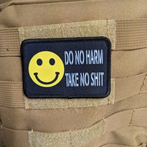 Pode incluir: Um remendo preto com um rosto sorridente amarelo e o texto "DO NO HARM TAKE NO SHIT" em branco.