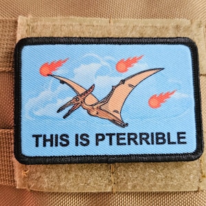 Puede incluir: Un parche azul y negro con un pterodáctilo de dibujos animados volando frente a un cielo azul con tres llamas rojas. El texto "THIS IS PTERRIBLE" está impreso en negro en la parte inferior del parche.