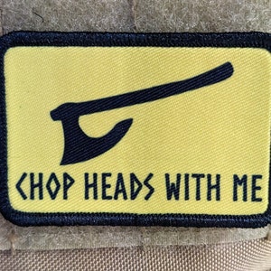May include: A yellow patch with black stitching and a black silhouette of an axe. The text "CHOP HEADS WITH ME" is printed in black below the axe.