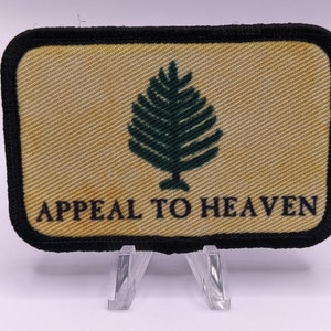 Puede incluir: Un parche rectangular negro y amarillo con un pino verde y el texto "APPEAL TO HEAVEN".