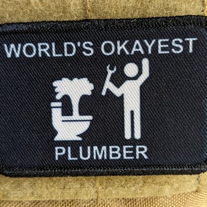 May include: Black and white patch with the text "WORLD'S OKAYEST PLUMBER" and a stick figure holding a wrench next to a toilet with a plunger coming out of it.