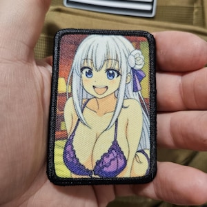 Peut inclure: Écusson rectangulaire avec une illustration de style anime d'une femme aux cheveux blancs et aux yeux bleus, portant un bikini violet. L'écusson a une bordure noire et est posé sur un fond beige.