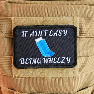 May include: A black and white patch with the text "It ain't easy being wheezy" and a blue inhaler graphic.