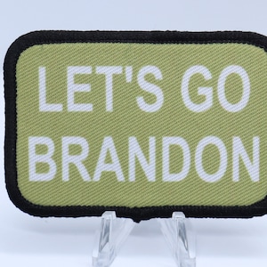 May include: A green and black rectangular patch with white text that reads "Let's Go Brandon".
