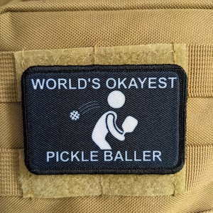 May include: Black and white patch with the text "World's Okayest Pickle Baller" and a white silhouette of a person playing pickleball.