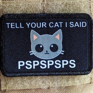 Puede incluir: Parche negro con texto blanco que dice "TELL YOUR CAT I SAID PSPSPSPS" y un gato gris de dibujos animados con orejas rosas y ojos negros.