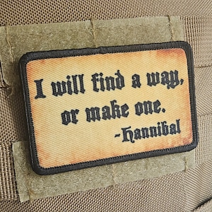 Op de afbeelding: Een beige stoffen patch met zwarte stiksels en een citaat in zwarte lettertypen dat luidt: "Ik zal een weg vinden, of er een maken. - Hannibal".