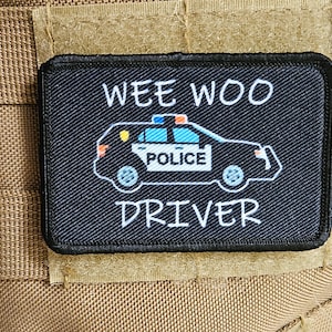 May include: Black patch with white text that reads "Wee Woo Driver". A cartoon police car with the word "Police" on the side is in the centre of the patch.