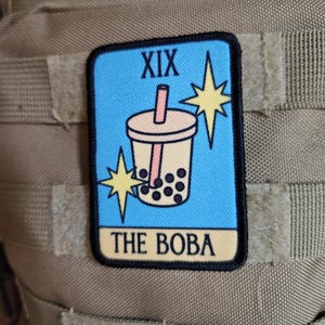 Könnte beinhalten: Rechteckiger Aufnäher mit einer Boba-Tee-Illustration und dem Text "XIX THE BOBA". Das Design umfasst einen hellblauen Hintergrund, eine Boba-Tee-Tasse und zwei gelbe Sternausbrüche.