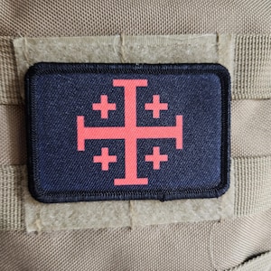 May include: A rectangular patch with a black border and a navy blue background. The patch features a red Jerusalem cross design. The patch is attached to a tan fabric surface.
