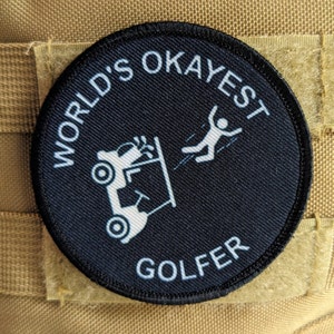 May include: A black and white embroidered patch with the text "World's Okayest Golfer" and a cartoon image of a golf cart with a person falling out of it.