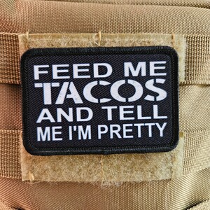 May include: Black and white patch with the text "Feed me tacos and tell me I'm pretty" on a tan background.