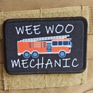 May include: Black patch with white text that reads "WEE WOO MECHANIC". A red fire engine with a ladder is pictured in the centre of the patch.