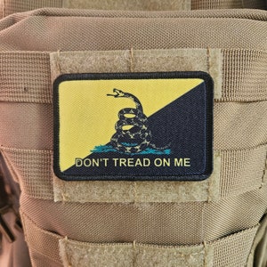 Puede incluir: Un parche negro y amarillo con una serpiente enroscada y el texto "DON'T TREAD ON ME".