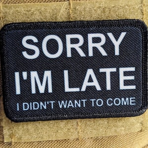以下が含まれることがあります： 「ごめんなさい、遅刻しました。来たくありませんでした。」と書かれた白い文字の黒いパッチ。
