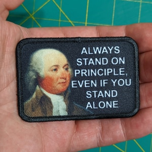 May include: Black and white embroidered patch with a portrait of a man and the text "ALWAYS STAND ON PRINCIPLE, EVEN IF YOU STAND ALONE".