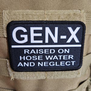 Puede incluir: Parche negro y blanco con el texto "GEN-X" en blanco, y el texto "RAISED ON HOSE WATER AND NEGLECT" en blanco debajo.