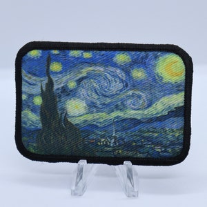 May include: A black framed patch with a printed image of Vincent van Gogh's "Starry Night" painting. The patch features a swirling blue sky with yellow stars and a dark green cypress tree in the foreground.