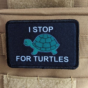 Pode incluir: Patch preto com texto branco que diz "I STOP FOR TURTLES". Uma tartaruga de desenho animado verde está no centro do patch.