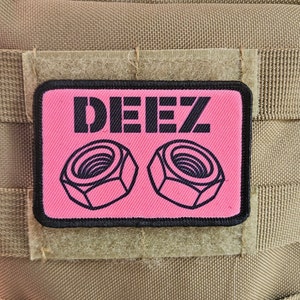 May include: A pink and black patch with the text "DEEZ" and two black outlines of nuts on a tan background.