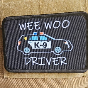 May include: Black patch with white text that reads "WEE WOO DRIVER". A cartoon police car with a "K-9" sign is in the center of the patch.
