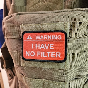 May include: A brown tactical backpack with a black patch that reads "WARNING I HAVE NO FILTER".