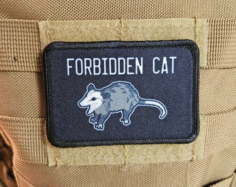 May include: A black patch with white text that reads "FORBIDDEN CAT" and a white and gray opossum illustration.