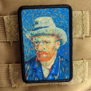 May include: A black and white embroidered patch featuring a portrait of Vincent van Gogh, with a blue background and a white hat. The patch is rectangular and has a black border.