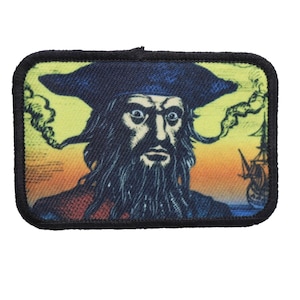 May include: A black and white embroidered patch of a pirate with a black hat and beard against a yellow, orange, and red sunset background. A ship is visible in the background.