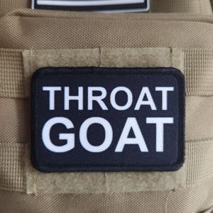 May include: A black patch with white text that reads "THROAT GOAT" on a tan background.