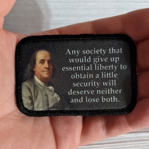 May include: A black patch with a portrait of Benjamin Franklin and a quote that reads: "Any society that would give up essential liberty to obtain a little security will deserve neither and lose both."