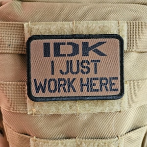 May include: A brown patch with black stitching and the text "IDK I JUST WORK HERE" in black letters.