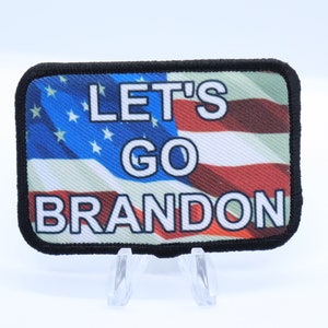 May include: A black and white patch with an American flag design and the text "Let's Go Brandon".