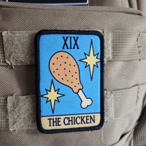 May include: A rectangular patch with a light blue background features a cartoon fried chicken leg, two yellow starbursts, and the Roman numeral XIX. The text "THE CHICKEN" is at the bottom. The patch is bordered in black.