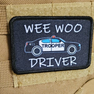 May include: Black patch with white text that reads "Wee Woo Driver". A cartoon police car with the word "Trooper" on the side is in the center of the patch.