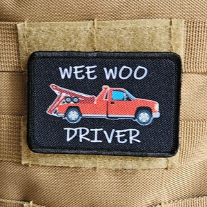 May include: A black and white patch with a red tow truck and the text "Wee Woo Driver".