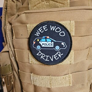 Może przedstawiać: Czarno-biała łatka z samochodem policyjnym i tekstem "Wee Woo Driver".
