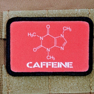 Könnte beinhalten: Ein roter Patch mit schwarzem Rand zeigt eine weiße chemische Struktur von Koffein und das Wort "CAFFEINE" in weißen Buchstaben.