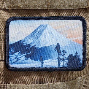 以下が含まれることがあります： 前景に木々のある山が描かれた青と白の刺繍パッチ。山は富士山を模したスタイリッシュなデザインです。