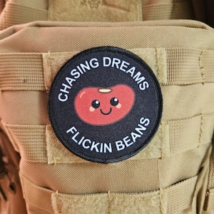 Könnte beinhalten: Ein schwarz-weißes Patch mit einem roten Bohnendesign. Das Patch sagt "Chasing Dreams Flickin Beans".
