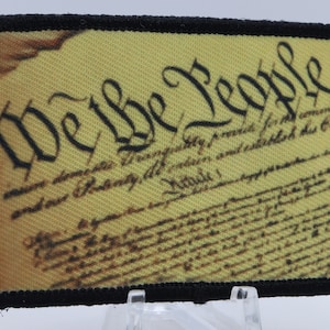 以下が含まれることがあります： 「We the People」というテキストと、色あせたアメリカ合衆国憲法の画像が描かれた黒と黄色のパッチ